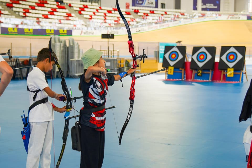 İki sporcu atış hattında; arkada numaralı hedefler