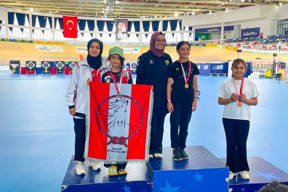 Kürsüde madalyalı sporcular; ortada Aşkar bayrağı